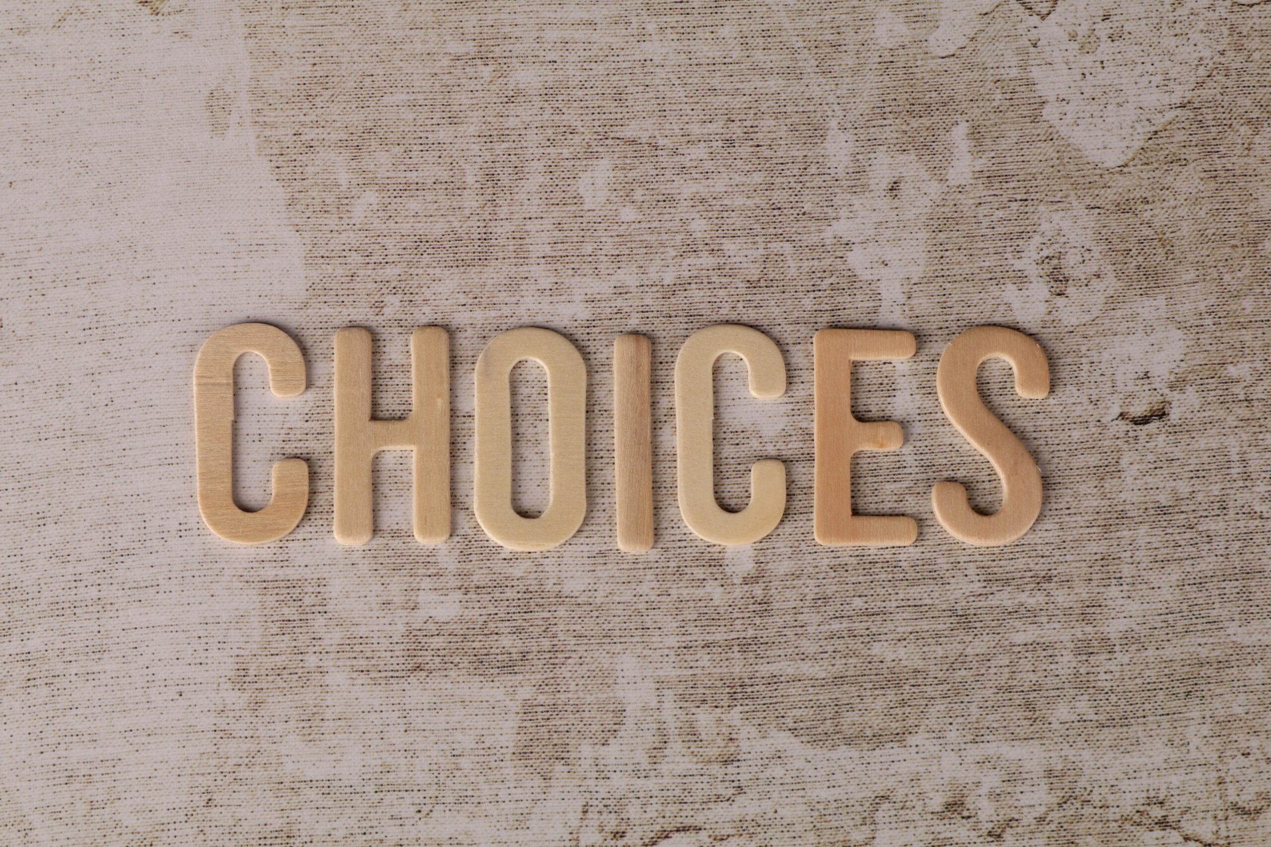 Wooden letters spelling 'choices' on a textured surface, symbolizing decision-making.