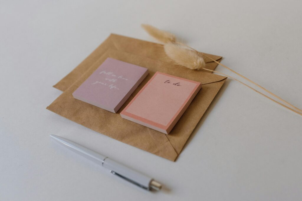 Aesthetic flat lay of sticky notes, pen, and brown envelope on white background.